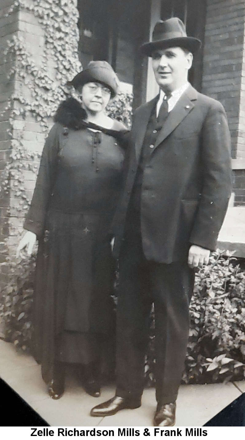 Black and white photo of Zelle Richardson Mills in dark floppy hat and dark dress with fur collar, wearing wire-rim glasses, standing next to her husband Frank Mills, a tall man wearing a homburg hat and black three-piece suit, in front of a brick house with ivy growing up the porch pillar.